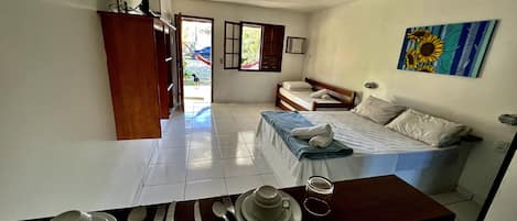 A room with a bed, a dining table set with cutlery, a ceiling fan, and a painting on the wall.