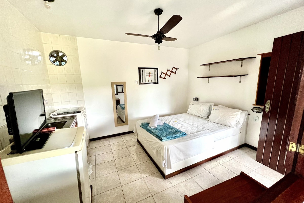 A small, clean room with a bed, a desk with a computer, a ceiling fan, and a small window.
