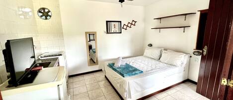 A small, clean room with a bed, a desk with a computer, a ceiling fan, and a small window.