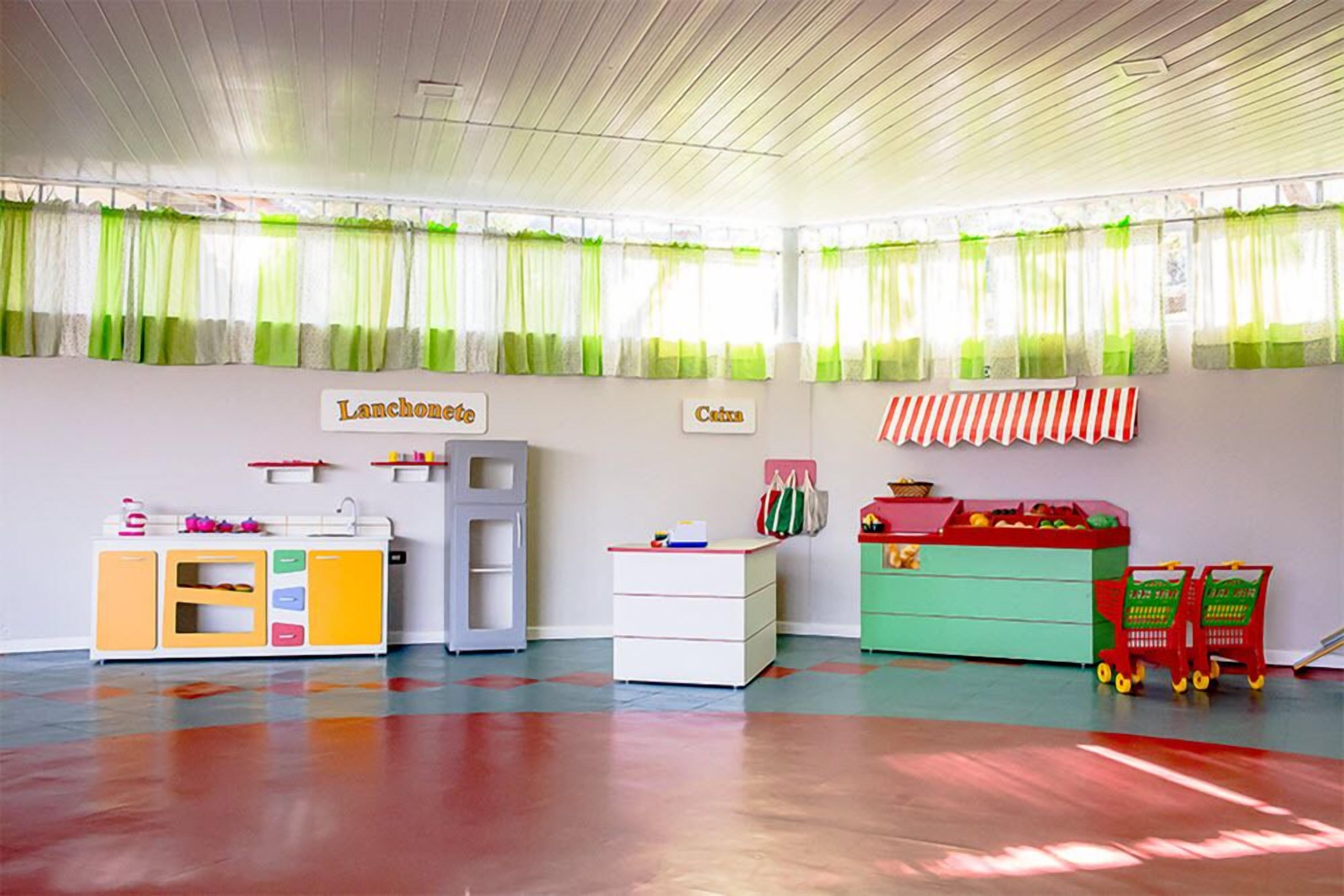 Een kleurrijke kinderspeelkamer met een speelkeuken, opbergmeubels en een speelgoedwagen.