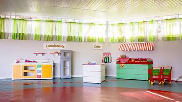 Een kleurrijke kinderspeelkamer met een speelkeuken, opbergmeubels en een speelgoedwagen.
