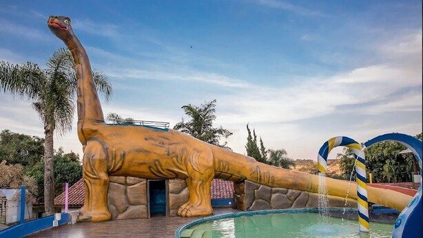 Ein wasserpark mit Dinosaurier-Motto, der ein großes aufblasbares Dinosauriermodell, einen Pool und eine Rutsche zeigt.