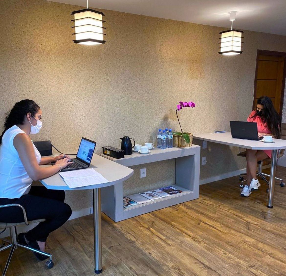 A reception area with two receptionists at desks, a coffee machine, water bottles, and a vase with flowers.