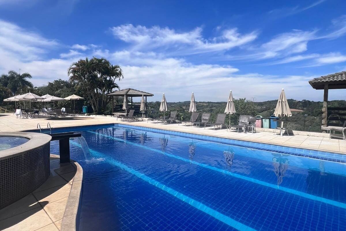 Ein klares, blaues Schwimmbecken mit Liegestühlen und Sonnenschirmen, umgeben von Bäumen und einem wolkenlosen Himmel.