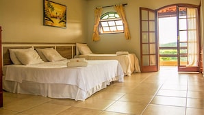 Ein Hotelzimmer mit zwei Betten, einem Gemälde an der Wand, einem Fenster mit Vorhängen und Blick durch eine offene Tür.