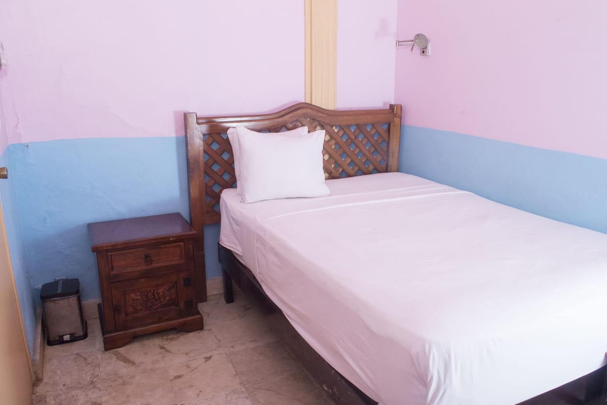 Ein Einzelbett mit Holz-Kopfteil, ein Nachttisch und ein kleiner Mülleimer in einem Zimmer mit blauen und rosa Wänden.