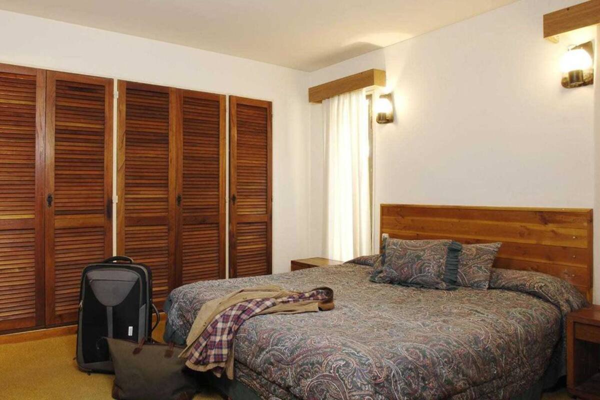 A bedroom with a bed, a suitcase, a nightstand, and a wardrobe with sliding doors.