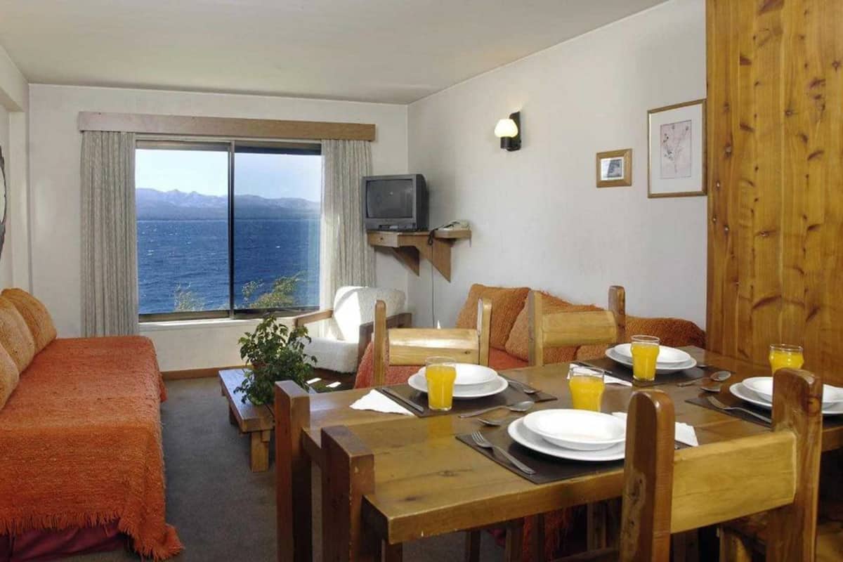 A cozy room with a wooden dining table set for two, a sofa, and a TV on a stand.