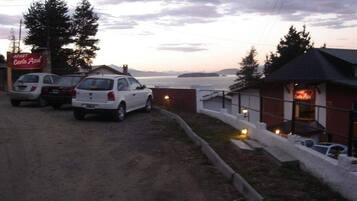 A parking area with two cars, a building with a sign 'Costa Azul', and a view of the sea and mountains in the background.