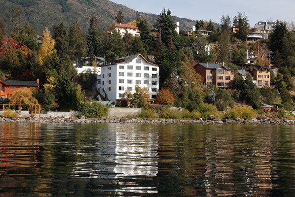 A lakeside hotel with a central white building surrounded by trees and other residential structures.