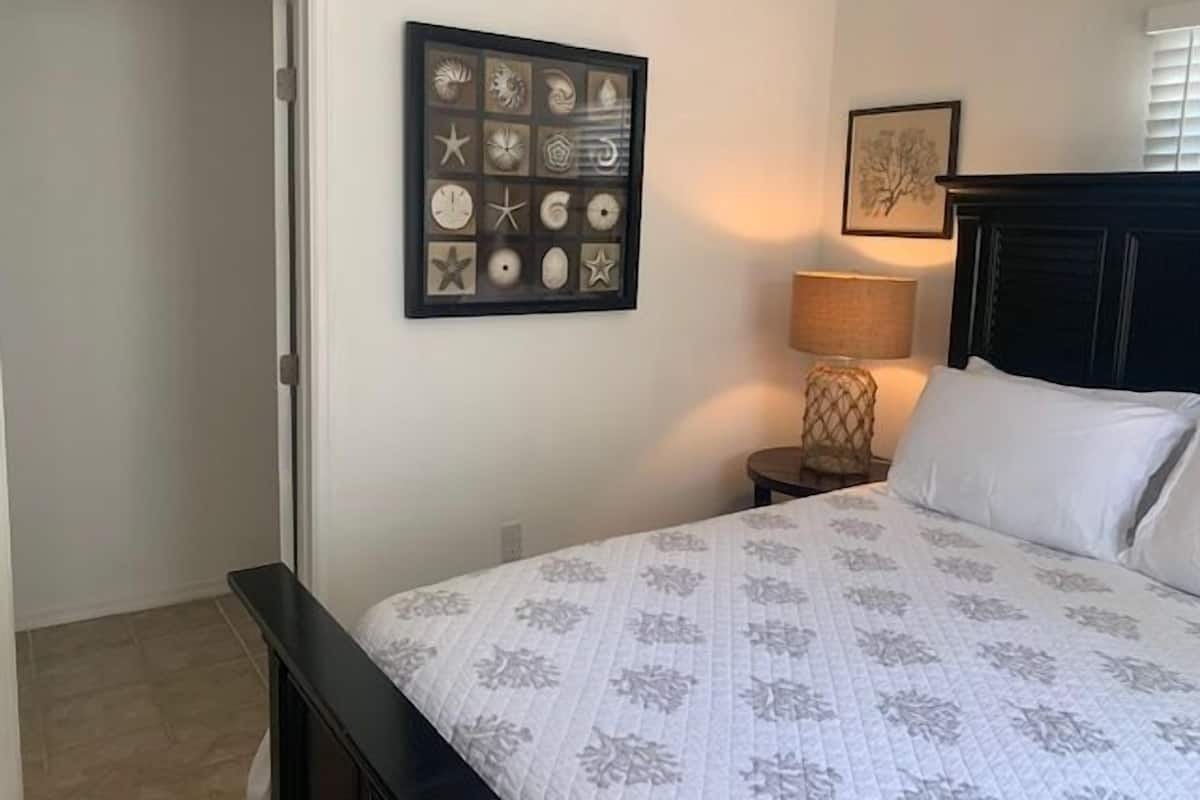 A bedroom with a bed, a nightstand, a lamp, and a framed picture of shells on the wall.