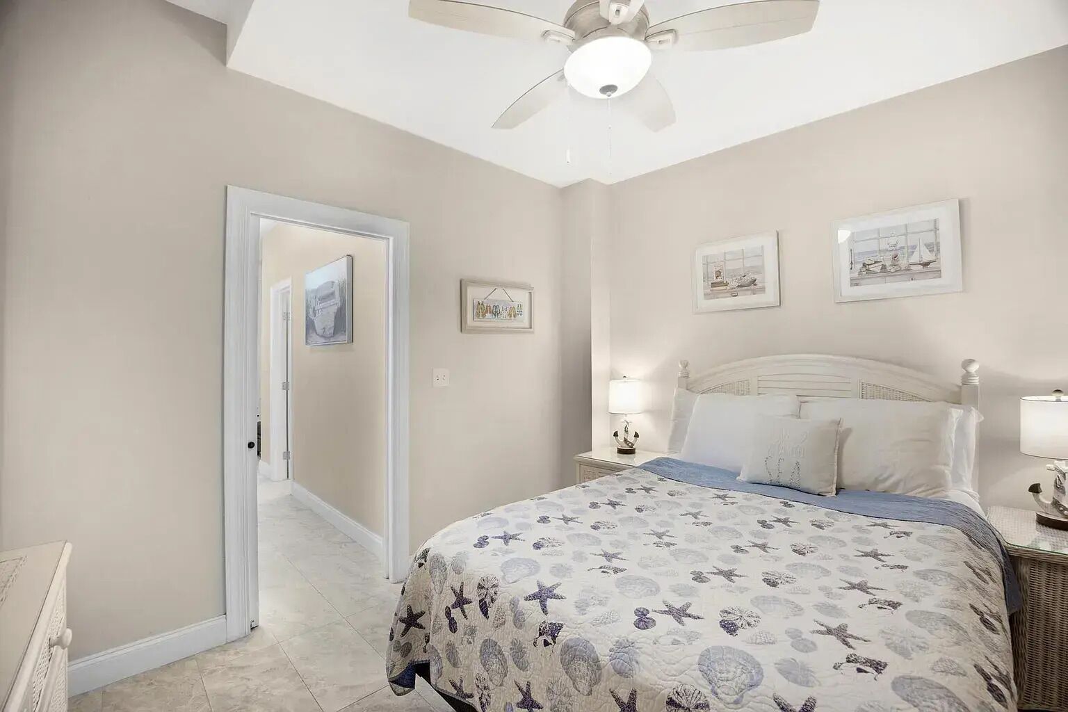 Un dormitorio con cama, mesita de noche, ventilador de techo y cuadros en la pared.