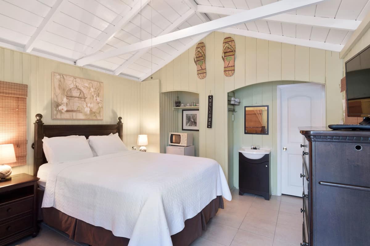 A bedroom with a large bed, a nightstand, a dresser, a vanity, and a television.