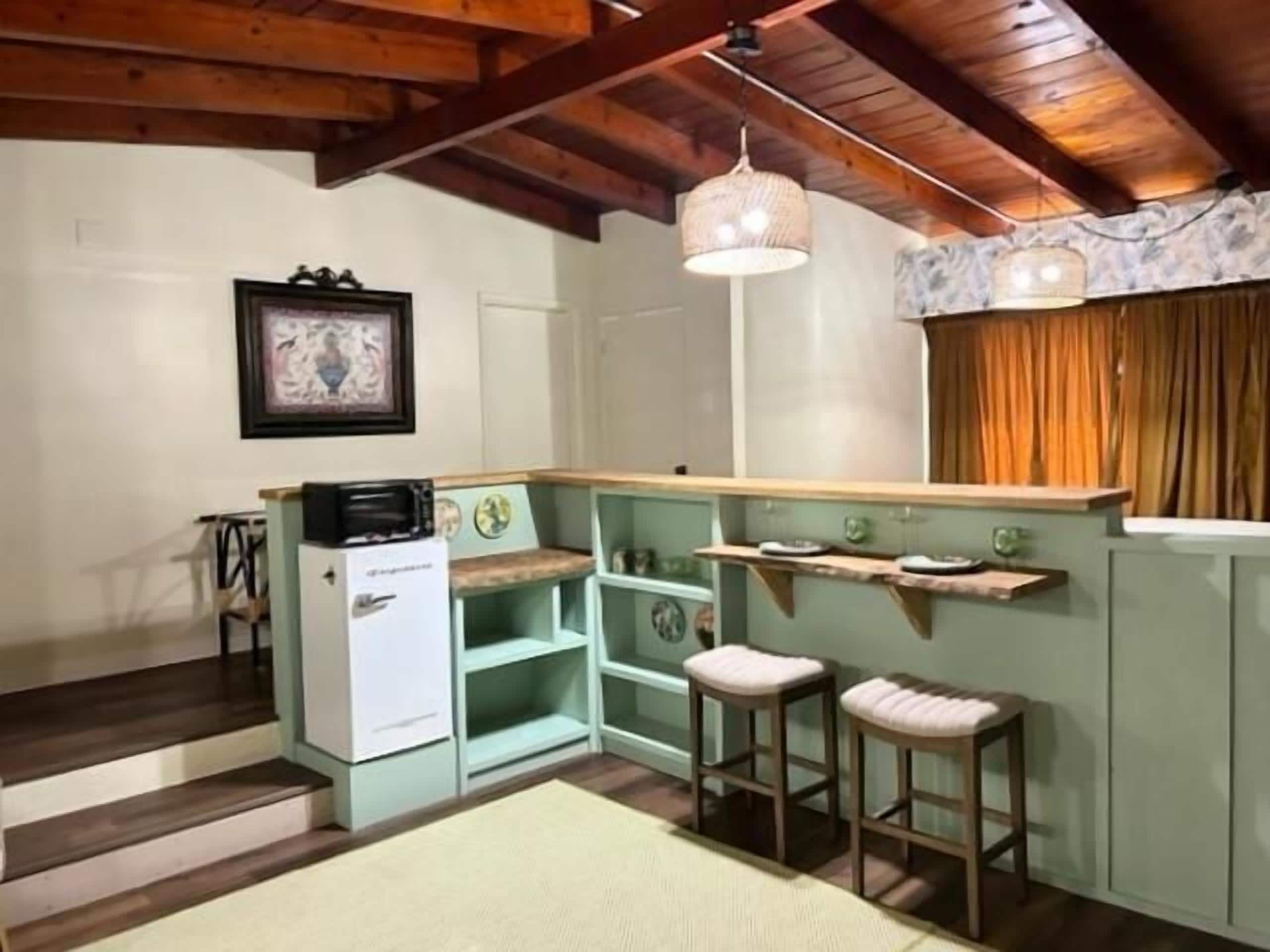 A compact kitchen with a wooden ceiling, a white refrigerator, and a small island with stools.