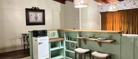 A compact kitchen with a wooden ceiling, a white refrigerator, and a small island with stools.
