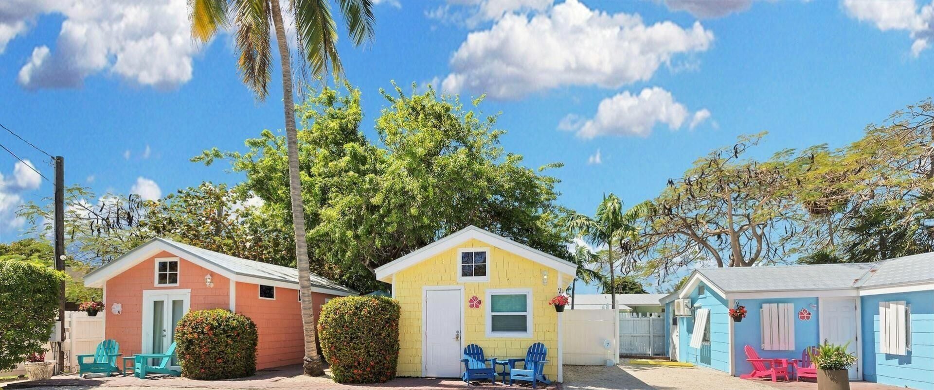 A row of colorful cabins with outdoor seating and a large tree in the background.