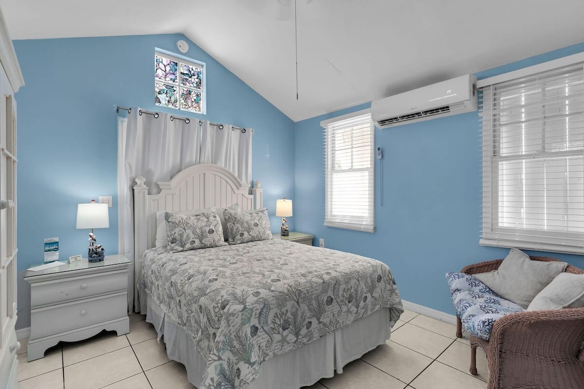 A bedroom with a bed, nightstands, a chair, and an air conditioning unit.