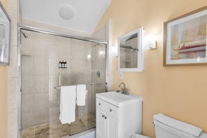 Un baño moderno con ducha de vidrio, lavamanos blanco y retrete.