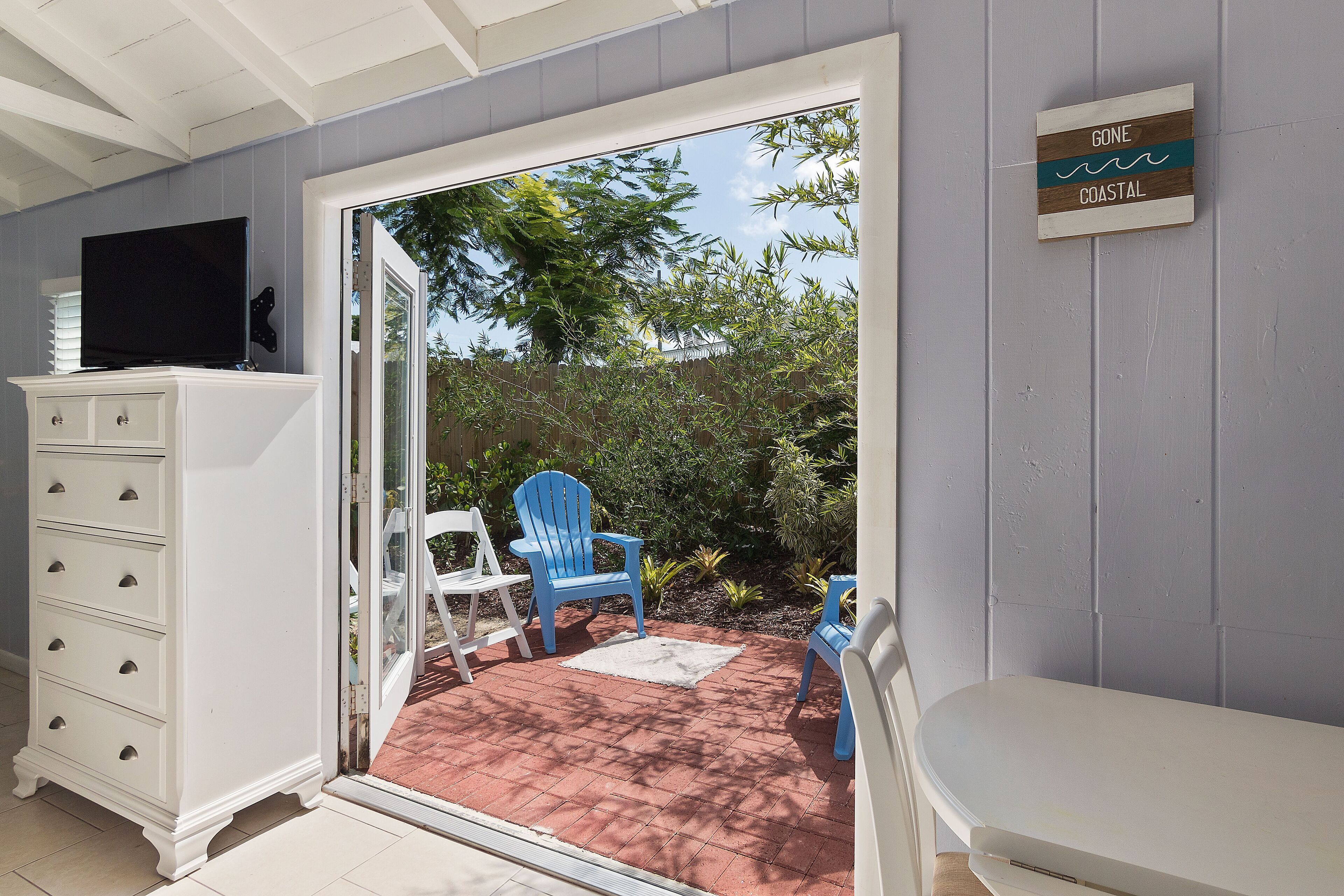 Een kamer met een schuifdeur die uitkomt op een patio met blauwe stoelen en een witte bank.