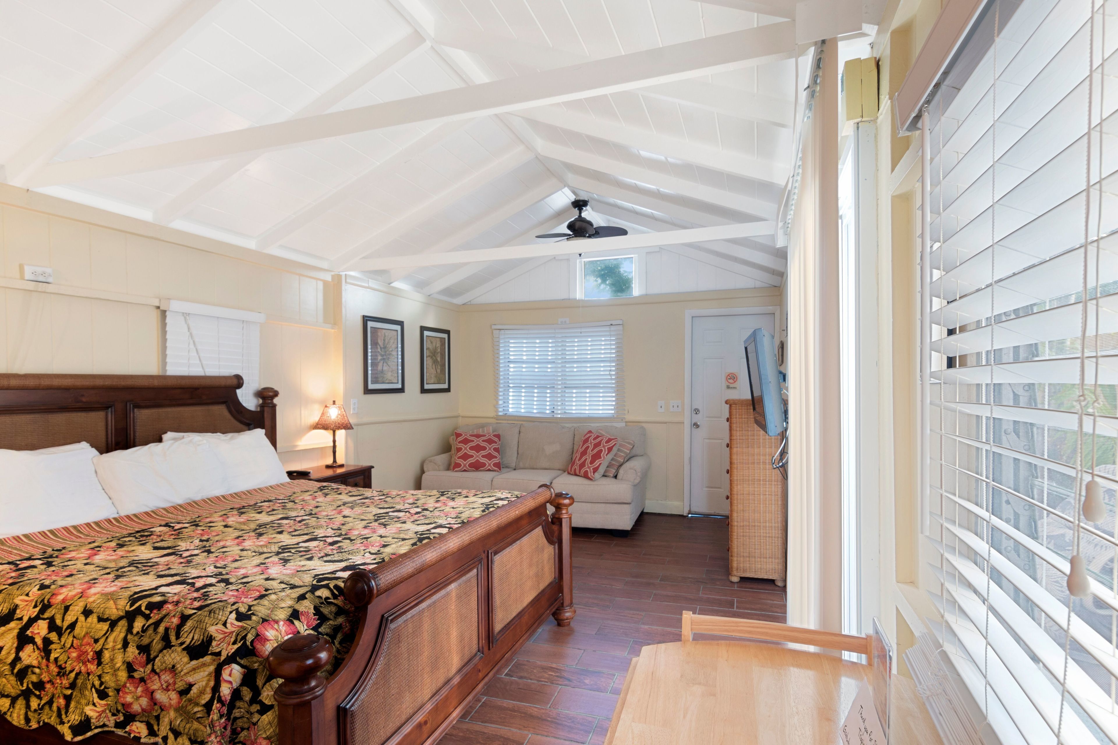 A bedroom with a wooden bed, a nightstand, a lamp, a window with blinds, and a ceiling fan.