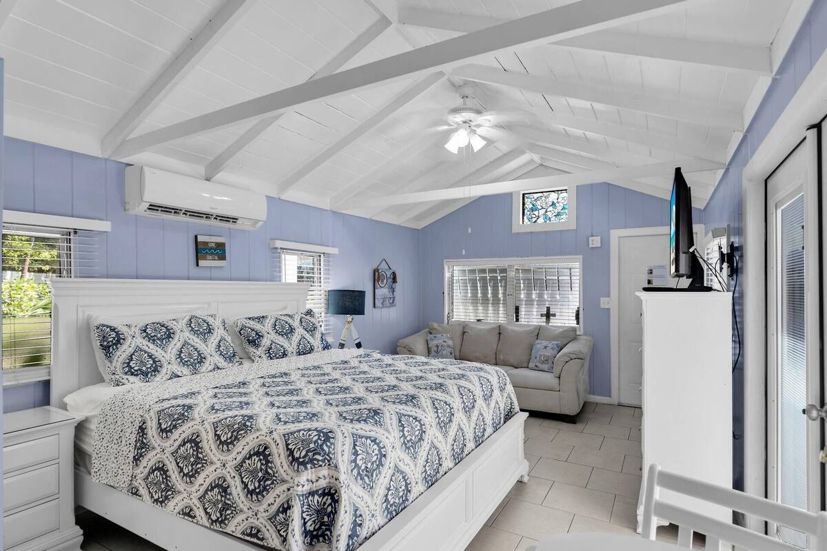 A bedroom with a large bed, a sofa, a TV, and a ceiling fan.