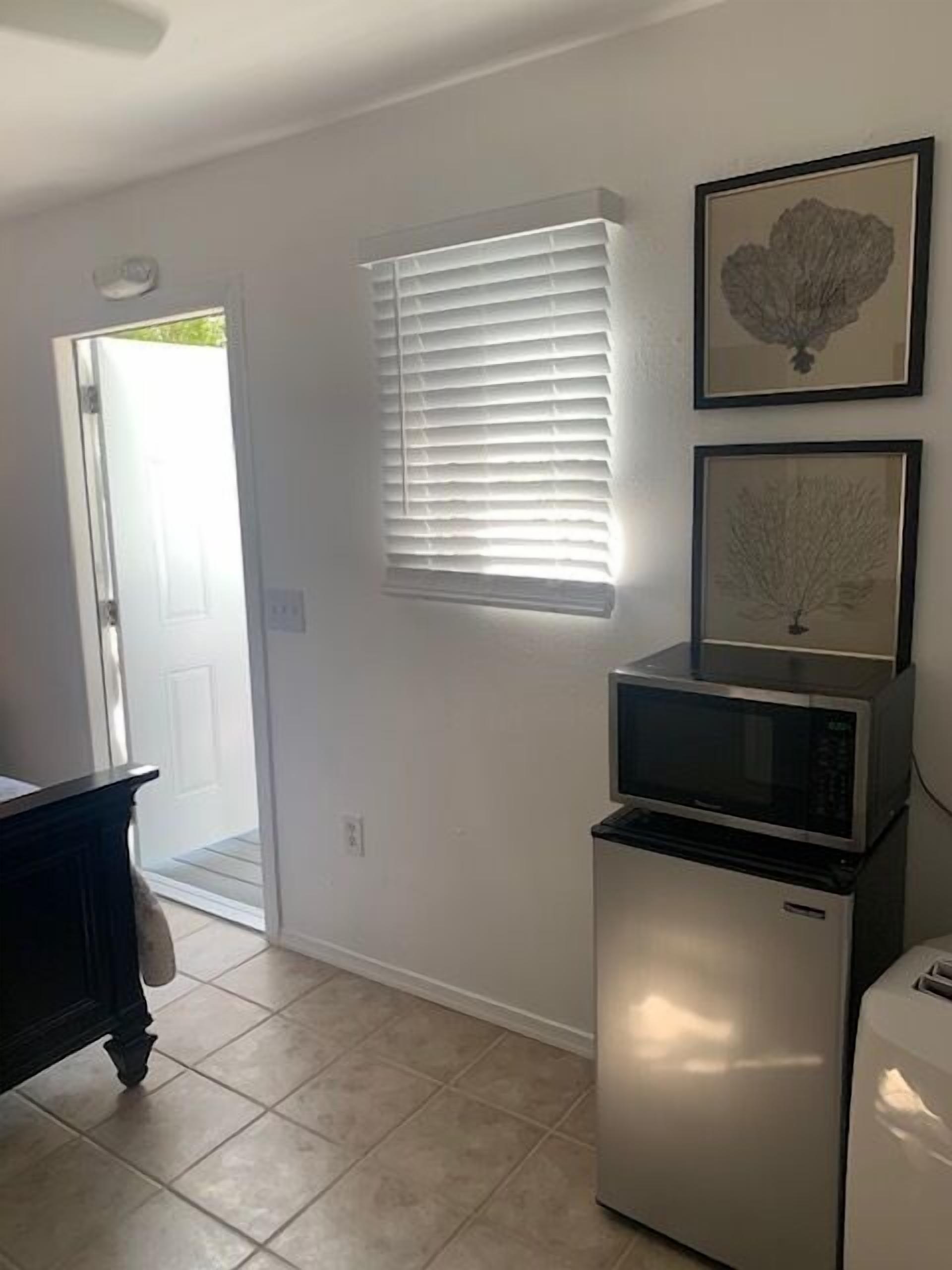 A kitchen with a microwave, refrigerator, and a door leading to an outdoor area.