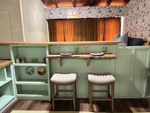 Una cocina con encimera de madera, dos taburetes y una ventana con cortinas.