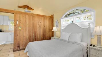 Un dormitorio con cama, una mesita de noche, una lámpara, una ventana con persianas y una puerta de madera.