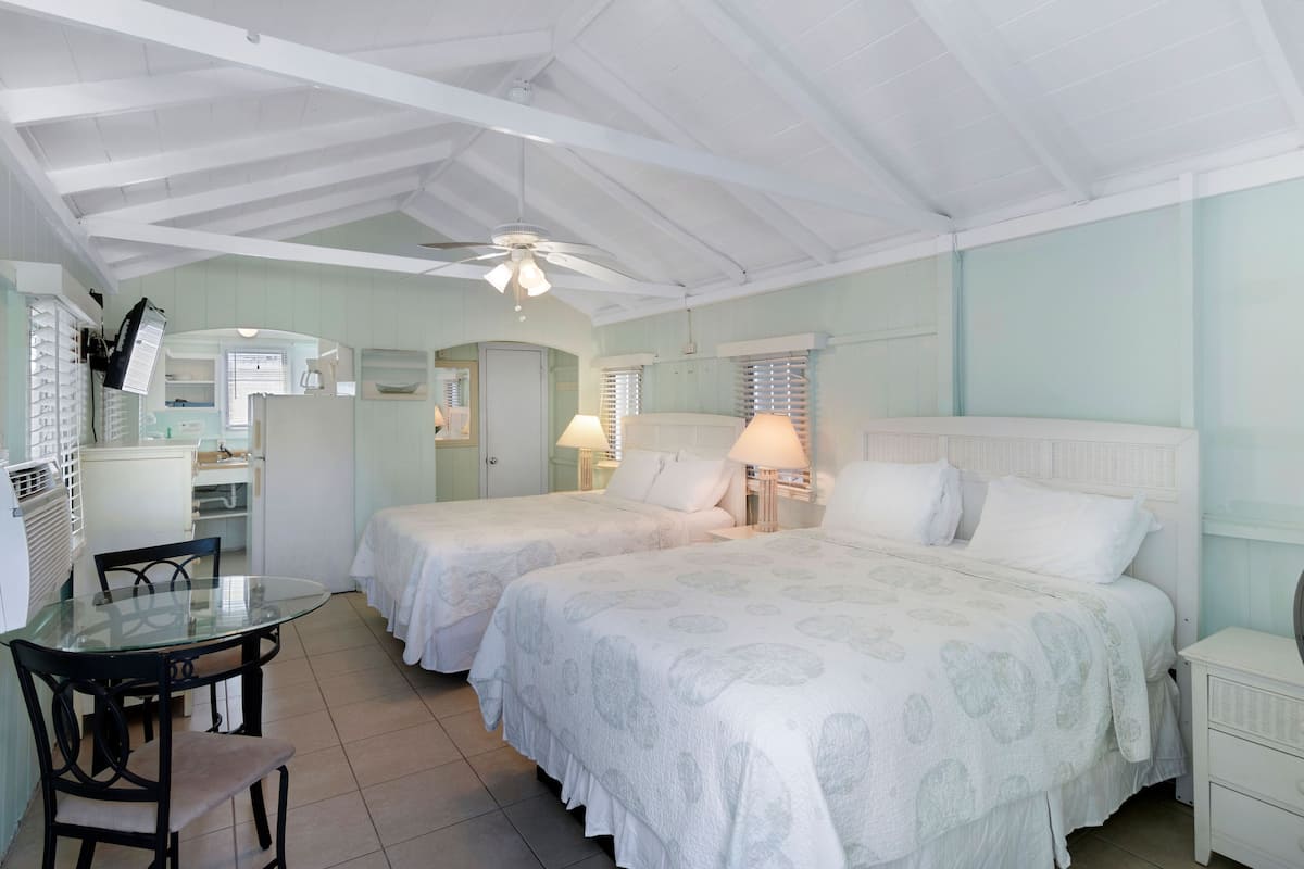A room with two beds, a dining table, and a kitchenette.