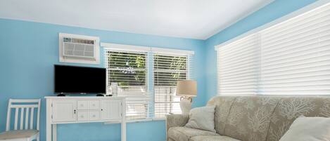 A living room with a blue wall, white furniture, a beige sofa, and a TV on a white cabinet.
