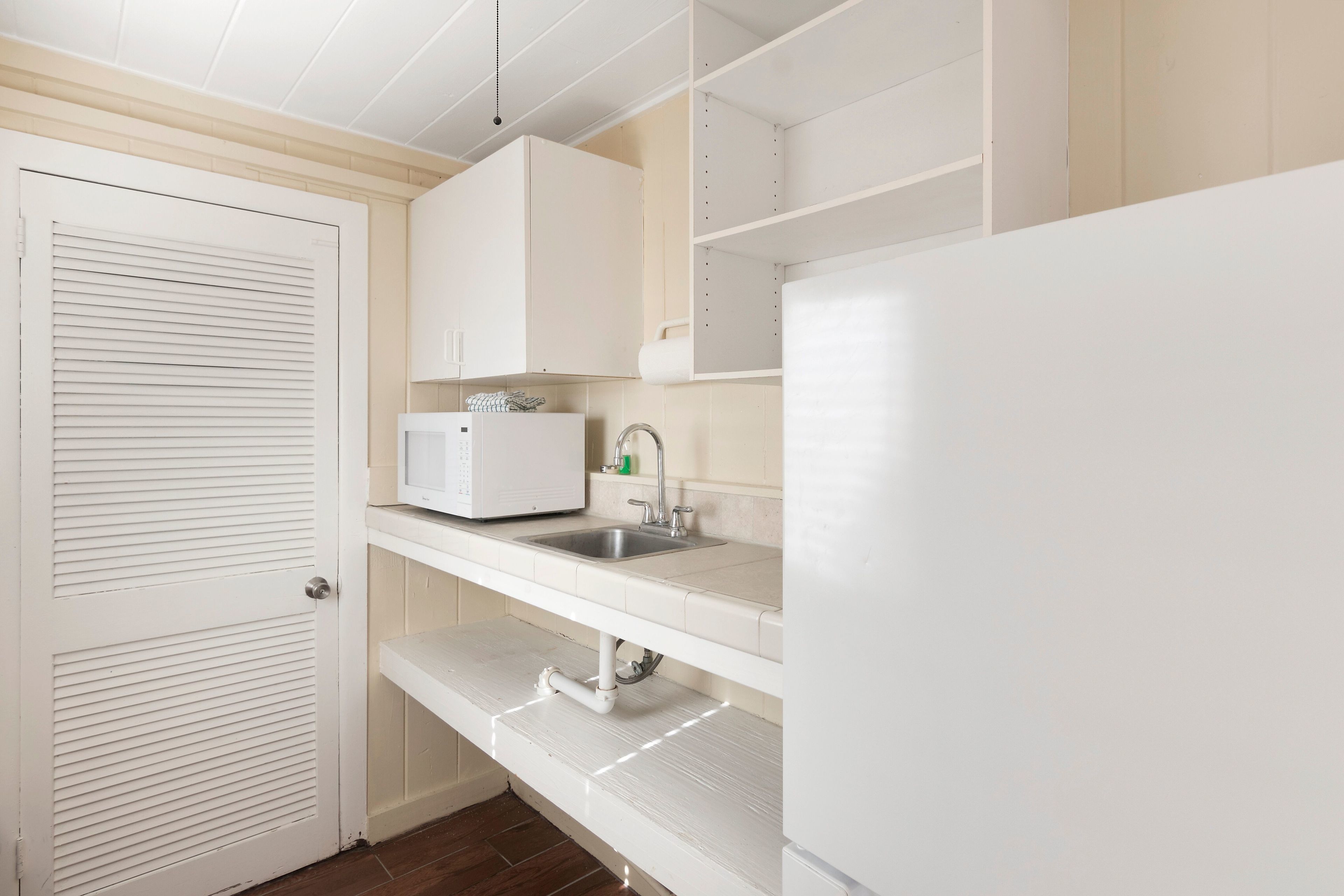 Cocina compacta con muebles blancos, horno microondas integrado, pileta y encimera blanca.
