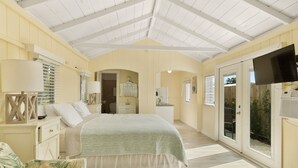 Un dormitorio con cama, mesitas de noche, televisor y puerta corrediza de cristal al exterior.