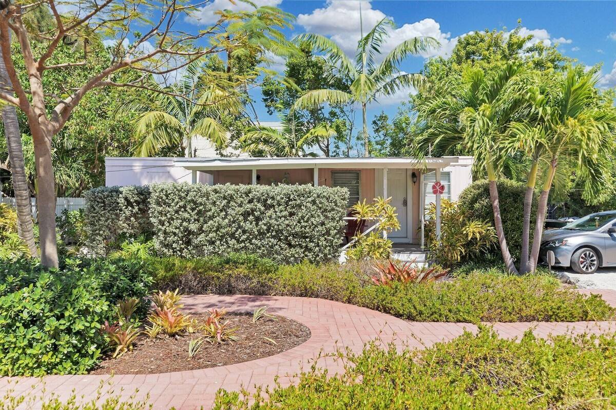 A small, single-story building with a covered porch, surrounded by lush greenery and palm trees.