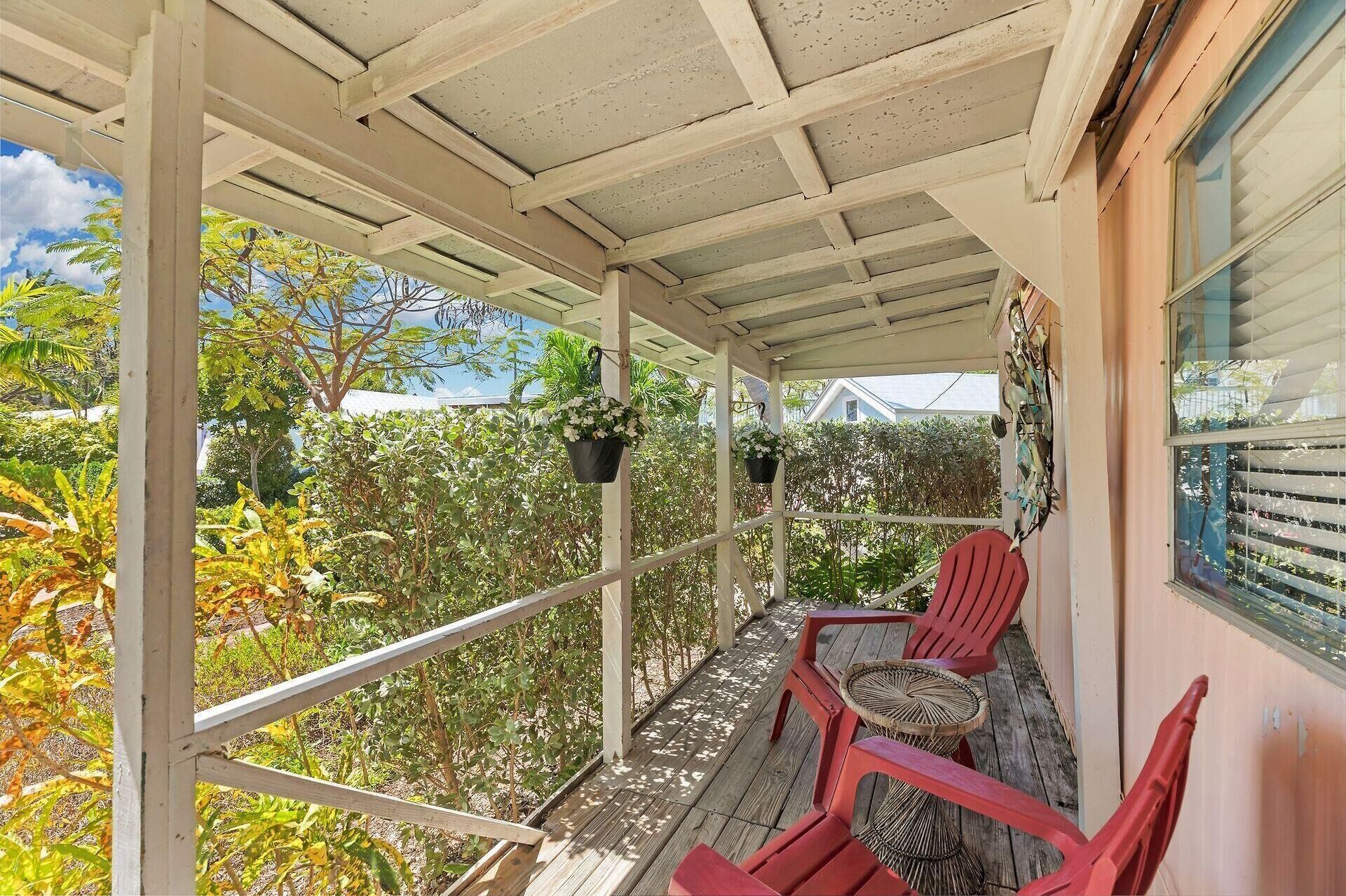 Ein überdachter Balkon mit Holzboden, roten Stühlen und hängenden Blumentöpfen.