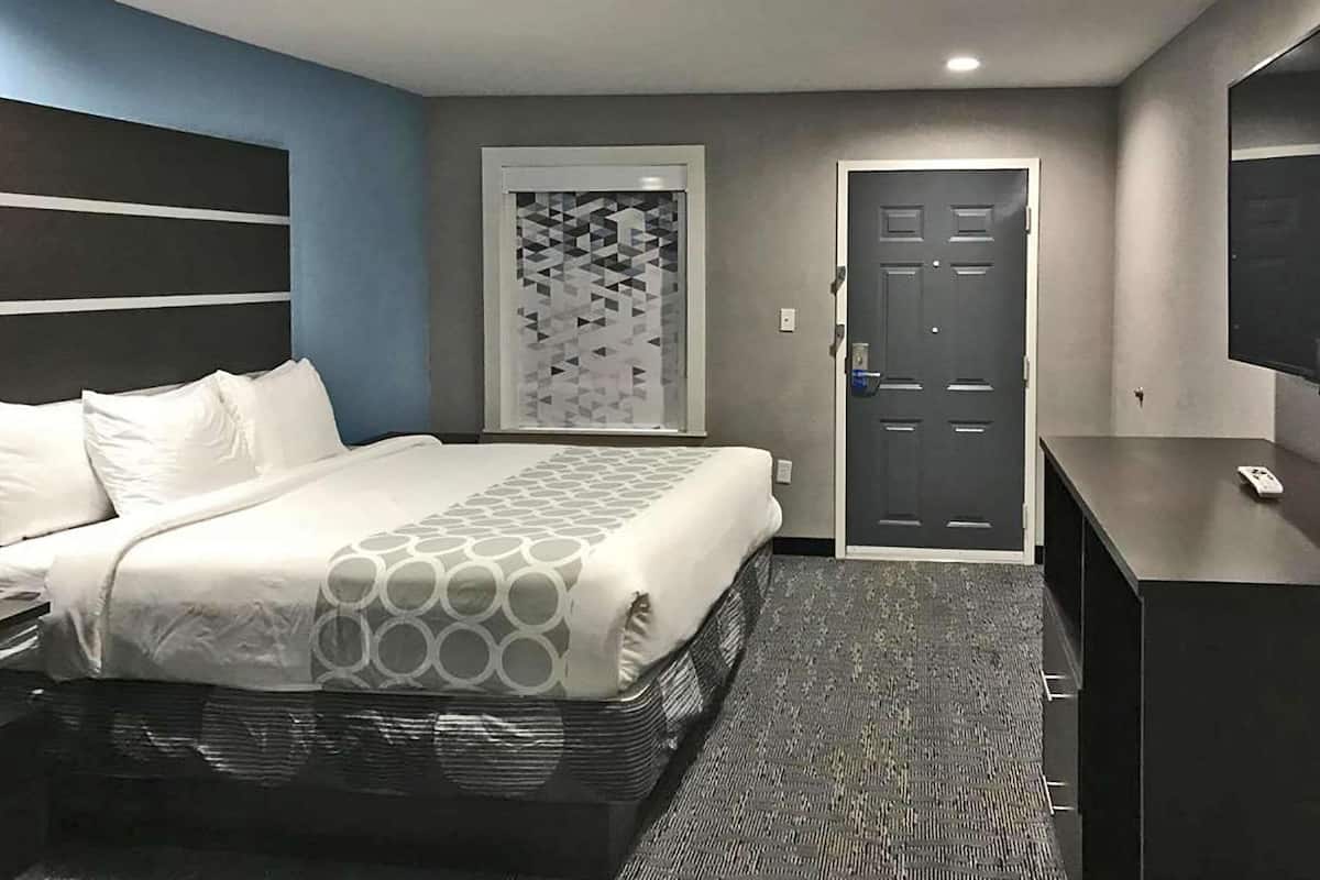 A hotel room with a bed, a desk, a door, and a wall-mounted TV.