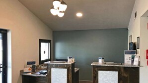 A reception area with two counters, a dark wooden desk, a large window, and a ceiling light fixture. - Rodeway Inn Calhoun South (Calhoun)