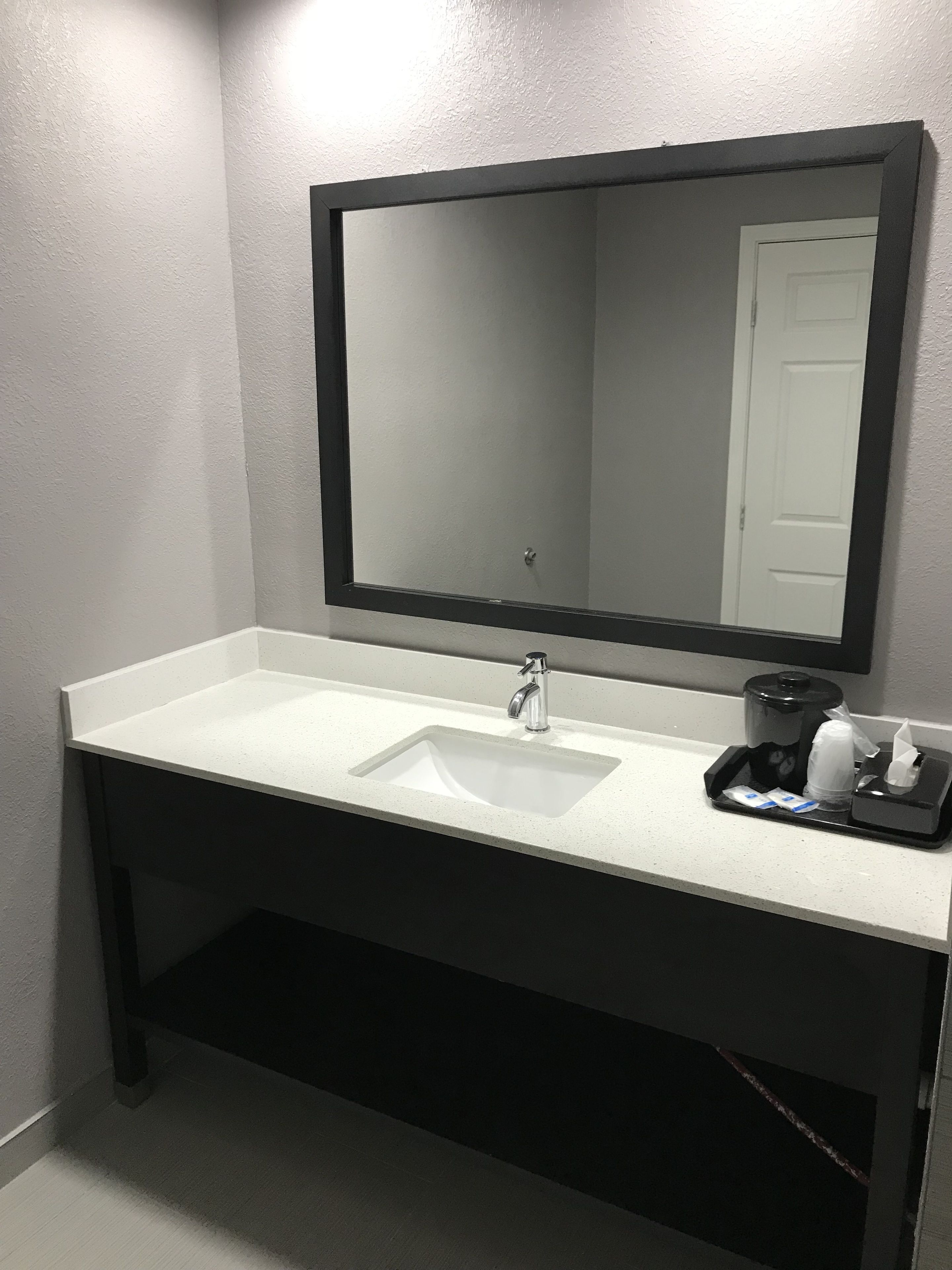 A bathroom with a white sink, a large mirror, and a black tray with toiletries.