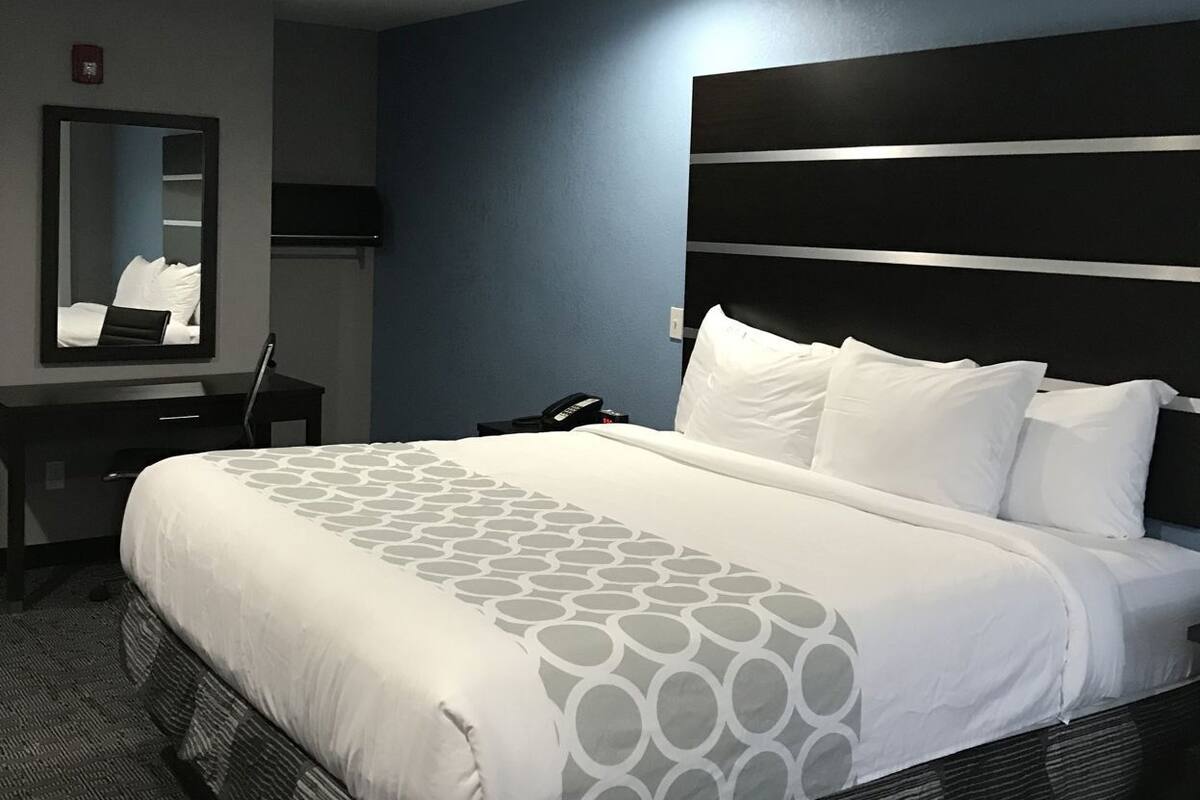 A hotel room with a bed, a desk, a chair, a mirror, and a telephone.