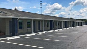 A motel with a row of single-story rooms, a covered parking area, and a clear sky. - Rodeway Inn Calhoun South (Calhoun)