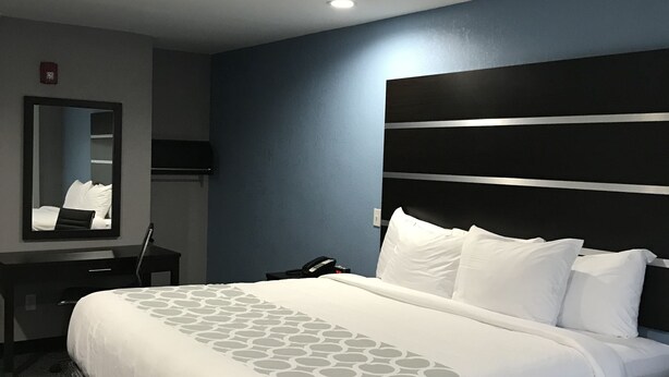 A hotel room with a large bed, a bedside table, a mirror, and a phone. - Rodeway Inn Calhoun South (Calhoun)