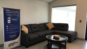 A modern hotel lobby with a dark-colored sofa, a glass coffee table, and a promotional banner. - Rodeway Inn Calhoun South (Calhoun)