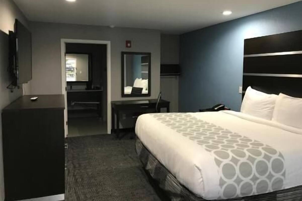 A hotel room with a bed, a desk, a chair, a TV, and a mirror.