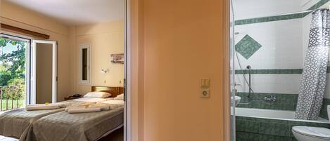 A hotel room with two beds, a bathroom with a shower and toilet, and a balcony with a view.