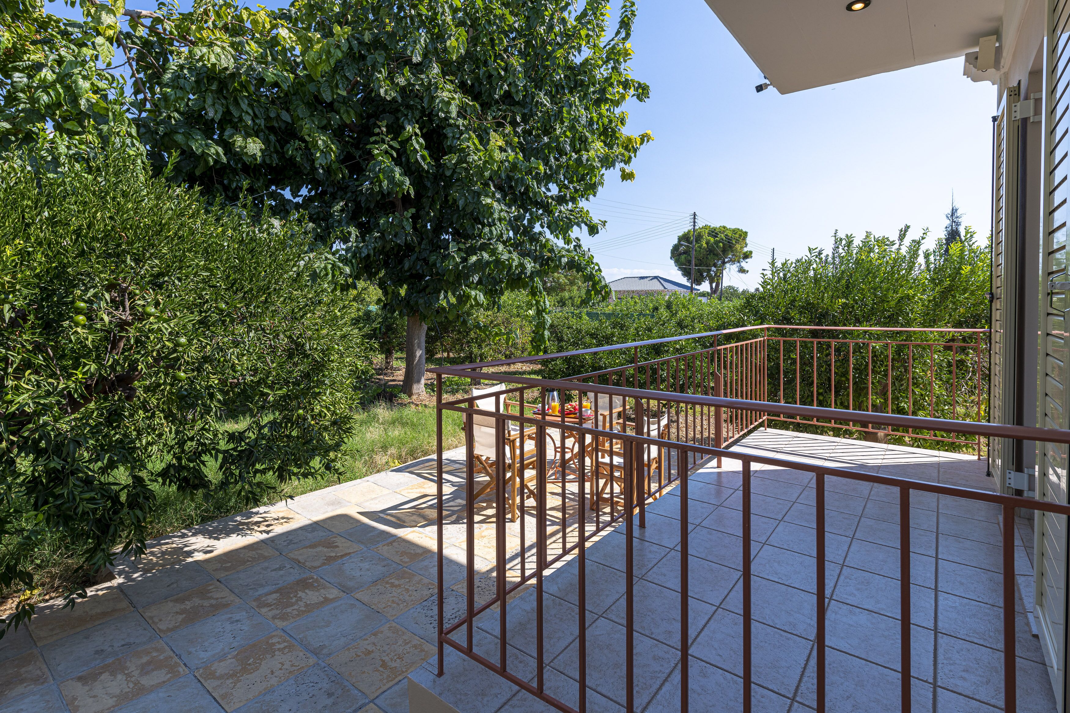 A balcony with a metal railing, a tiled floor, and a view of a tree and greenery.