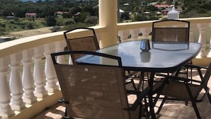 A balcony with a glass table and chairs, offering a view of a mountainous landscape and a body of water. - Williams Estate (Falmouth Harbour)