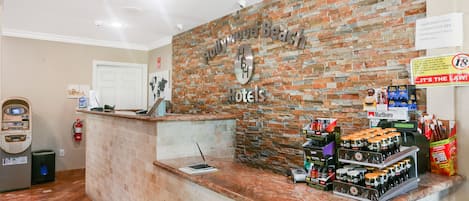 A reception area with a brick wall, a counter with a computer, and various items like a fire extinguisher and a sign about credit card minimum purchase.