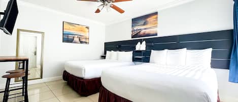 Habitación de hotel con cama, escritorio, silla, ventilador de techo y dos cuadros en la pared.