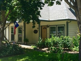 Uma casa com telhado empena e porta frontal, com uma bandeira do Texas.