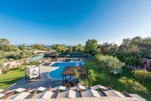 Zona de piscina con pérgola, sillones de descanso y vista al mar.