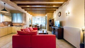 A cozy living room with a red sofa, wooden beams, a kitchen with yellow cabinets, and a TV on a wooden stand. - Villa Maxim with Private Pool & Tennis Court (Corfu)
